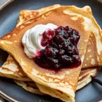 Golden Swedish Pancakes with Cream and Lingonberry Jam on a Rustic Plate